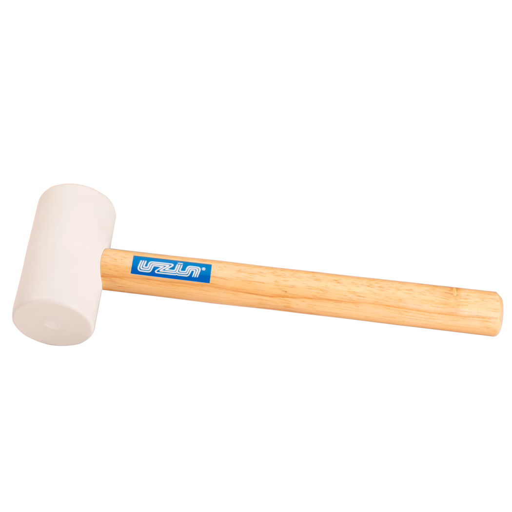 UZIN_Dummy_rubber hammer-UZIN_2014-11 Nærbilde av et gummihammer-produkt: lys beige gummihode montert på et glatt lyst treskaft med en blå rektangulær merkeetikett; hammeren ligger diagonalt på en ren hvit bakgrunn, myk jevn belysning fremhever gummitekstur og treets årringer; egnet for skånsomme slag ved trearbeid, montering eller flislegging.